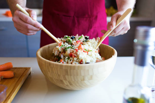 Handsome young man preparing quinoa salad with vegetables in the kitchen.