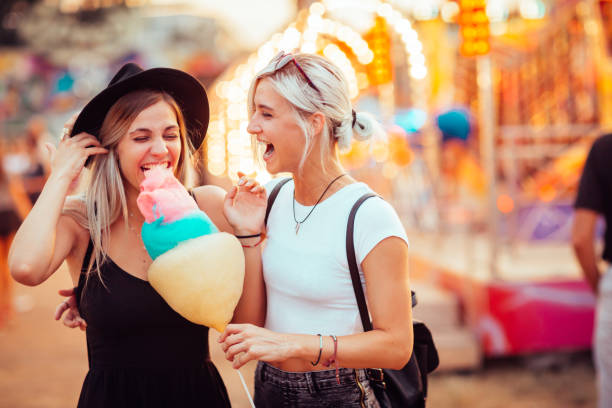 Friends in amusement park Shot of happy female friends in amusement park eating cotton candy. Two young women enjoying a day at amusement park. child cotton candy stock pictures, royalty-free photos & images