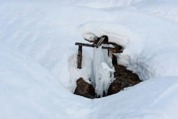 Photo of Rustic wooden chanel for mountain spring water covered with deep snow and ice