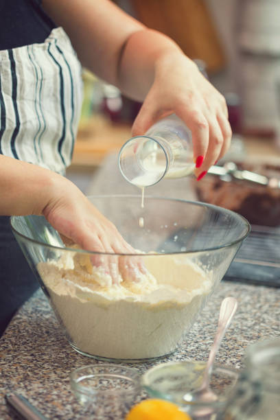 Young woman preparing donuts at home, she pouring milk into glass bowl