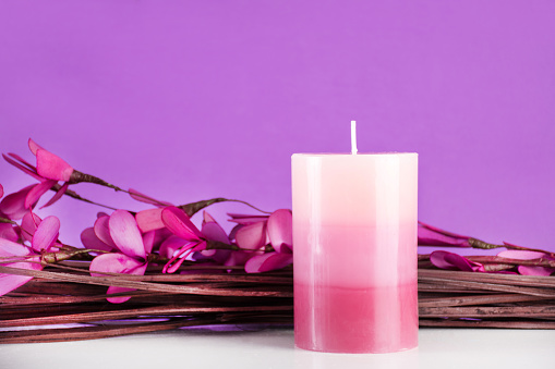 Beautiful gently spa composition with aromatic candle and purple flower and branches on desk and purple background. Decoration concept. Close up, selective focus