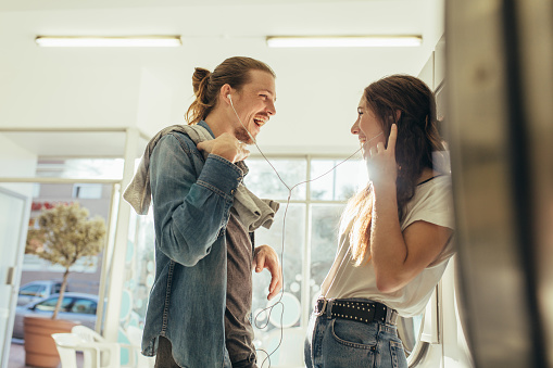 Couple sharing earphones listening to music standing at home. Couple in love having fun listening to music standing in laundry room.