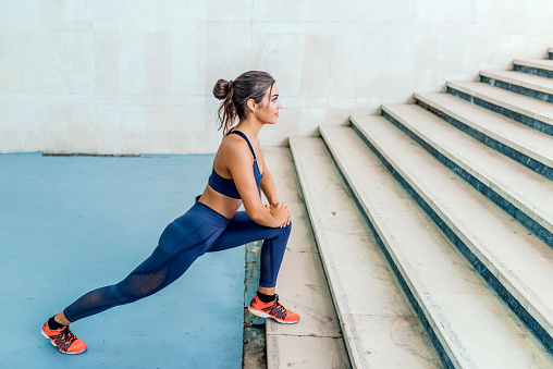 Photo of Fitness woman doing lunges exercises for leg muscle workout training, outdoors. Active girl doing front forward one leg step lunge exercise. Young beautiful woman doing leg stretching before running upstairs.