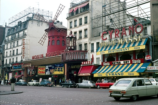 Pigalle, Paris, Il de France, France, 1972. Street scene on Boulevard de Clichy with the famous Moulin Rouge and Restaurant Cyrano. Furthermore: cars, traffic, pedestrians, buildings, advertising and cinema posters.
