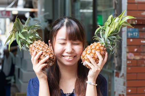 A girl gives a cheesy grin as she poses with two small pineapples