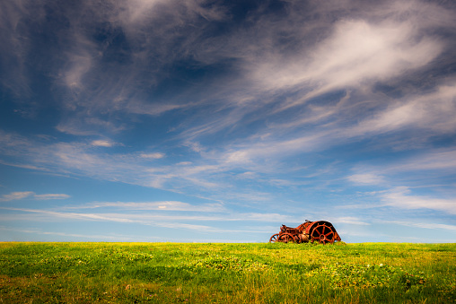 A rusty red tractor resting on the hill on a perfect spring day