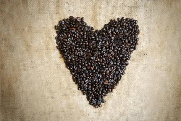 High angle view of roasted coffee beans shaped heart symbol above burlap fabric