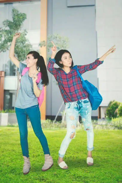 Portrait of excited college students celebrating their success by dancing together in the  park