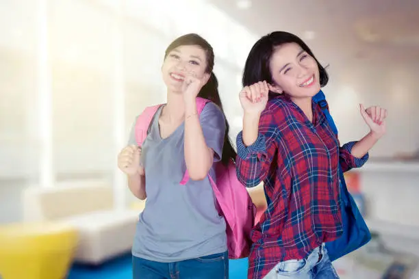 Excited female college students are carrying backpack while dancing together in the library