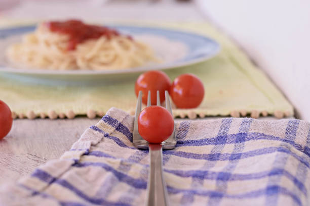 Closeup red fresh cherry tomato at silver fork whit pasta in background/ Italian food