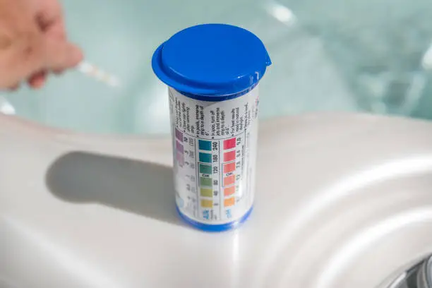 Photo of Test strips for spa hot tube water chemisty. Dipping hand in water.