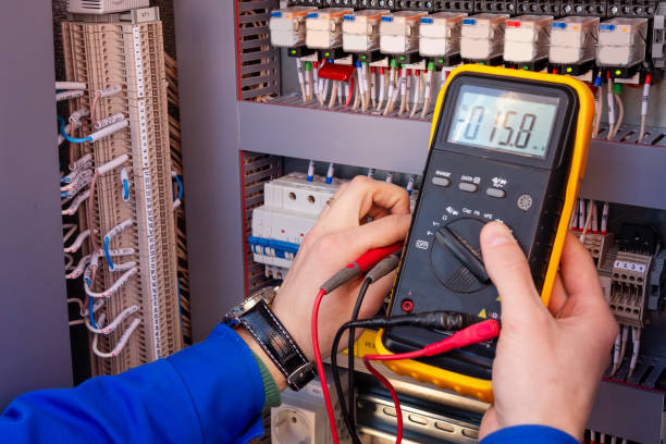 Multimeter in hands of electrician engineer in electrical cabinet. Maintenance of electric system. Worker tests of electrical circuit. Electrician with tester in hands. stock photo