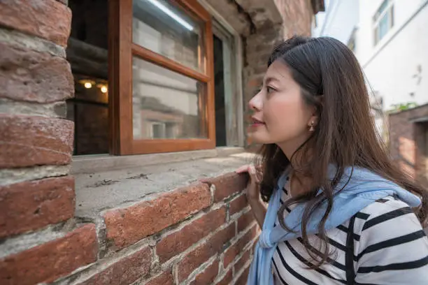 asian woman looking inside through the window. standing at the old house.