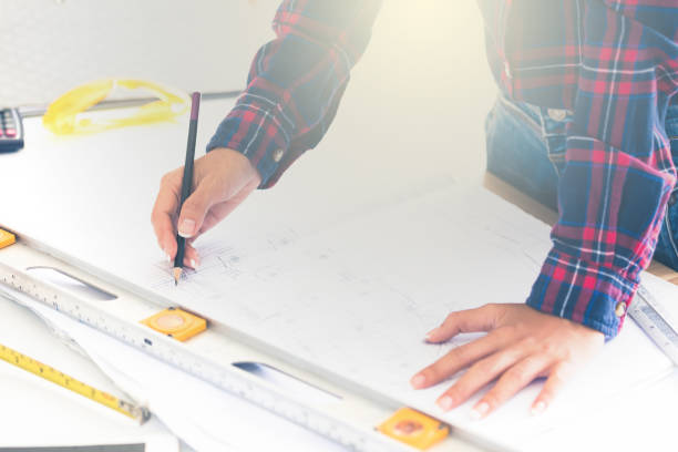 istock Hands of female architect or engineer using pencil working with blueprint on desk in office. 1040845944