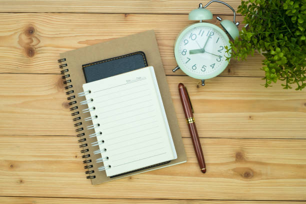 istock Office supplies or office work essential tools items on wooden desk in workplace, pen with notebook and alarm clock, top view 1040873078