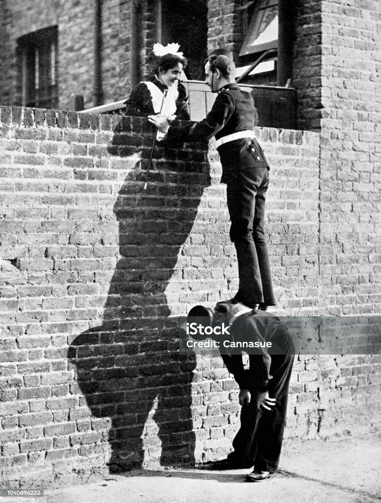 Victorian image of a soldier stood atop a sailors back so he can talk to a pretty lady atop a tall brick wall; 19th century humour ; from The Navy and Army Illustrated 1899 Taken from the Navy and Army Illustrated annual of 1899 Old-fashioned Stock Photo