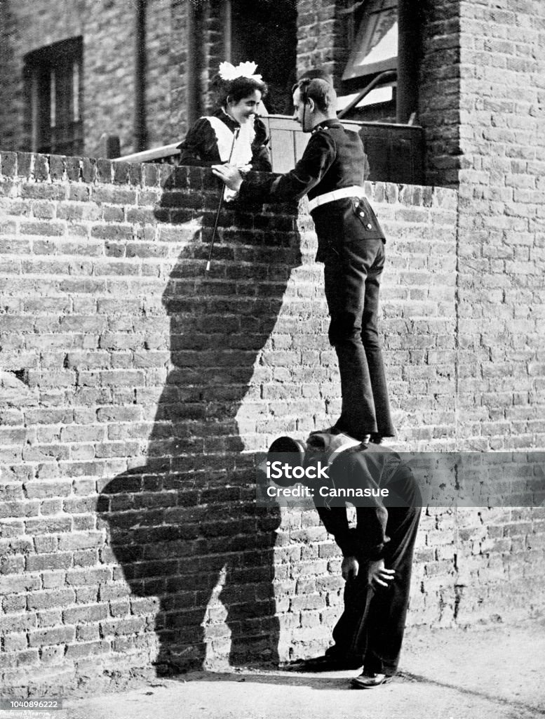 Victorian image of a soldier stood atop a sailors back so he can talk to a pretty lady atop a tall brick wall; 19th century humour ; from The Navy and Army Illustrated 1899 Taken from the Navy and Army Illustrated annual of 1899 Photography Stock Photo