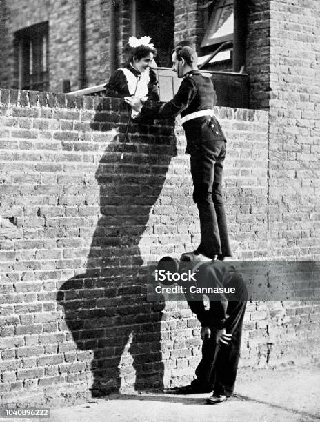 Victorian Image Of A Soldier Stood Atop A Sailors Back So He Can Talk To A Pretty Lady Atop A Tall Brick Wall 19th Century Humour From The Navy And Army Illustrated 1899 Stock Photo - Download Image Now