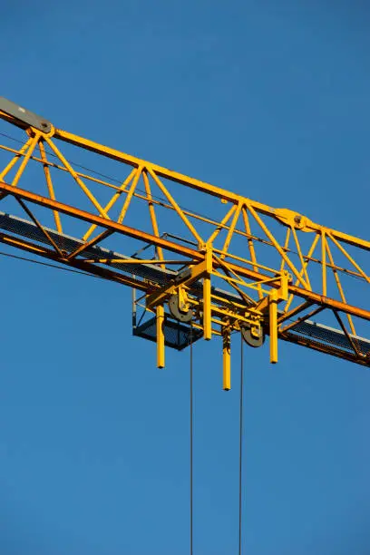 Details of a tower crane against the background of clear blue sky. Contrast of yellow paint and blue air. Metal frames and ropes. Construction or building concept. Free space to add text