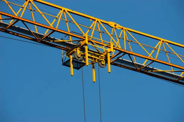 Details of a tower crane against the background of clear blue sky. Contrast of yellow paint and blue air. Metal frames and ropes. Construction or building concept. Free space to add text