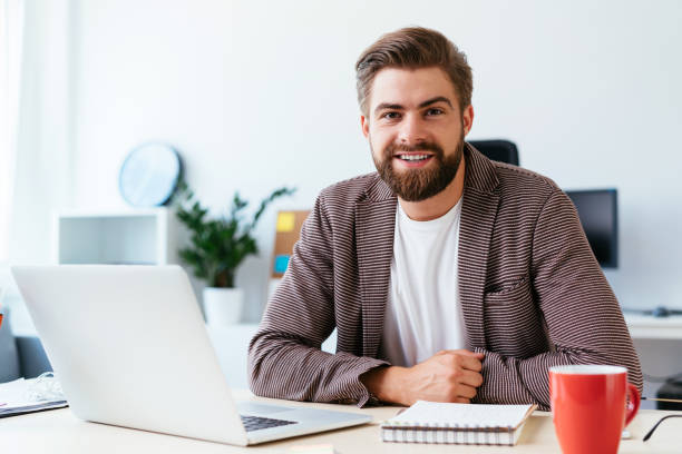 portrait d’homme d’affaires jeune startup assis dans le petit bureau moderne et regardant la caméra - internet student business men photos et images de collection