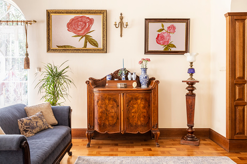 Foto real de un antiguo mueble con adornos de porcelana, cuadros con rosas y azul sofá en una sala de estar interior photo