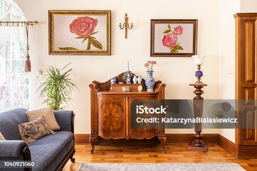 istock Real photo of an antique cabinet with porcelain decorations, paintings with roses and blue sofa in a living room interior 1040921060