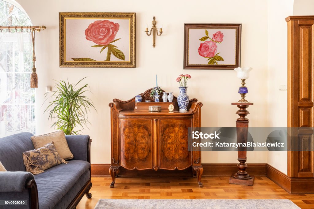 Real photo of an antique cabinet with porcelain decorations, paintings with roses and blue sofa in a living room interior Old Stock Photo
