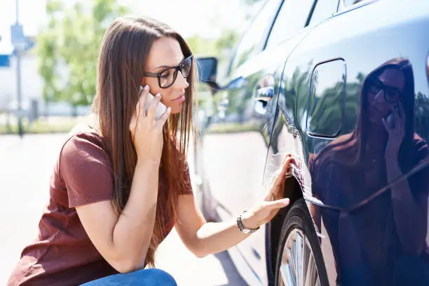 Photo of Yougn woman inspecting her scratched car and calling insurance agent