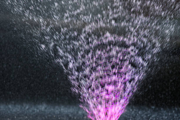 Illuminated water jets of a fountain. Violet color, dark background. Texture or background