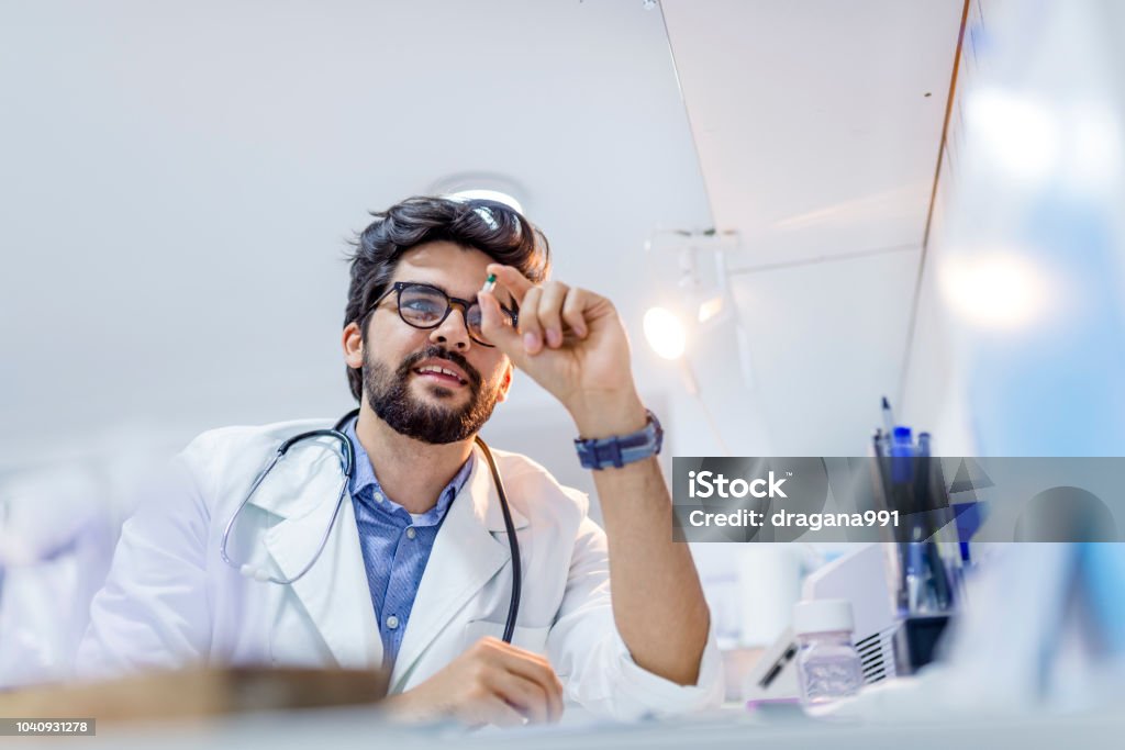 Young attractive male scientist holding a  pill. Young attractive male scientist holding a  pill. Male doctor holding a pill. Pharmacist holding a pill. Hand of a hospital medical expert shows the pill to be taken to his patient. concept of generical pills Nutritional Supplement Stock Photo