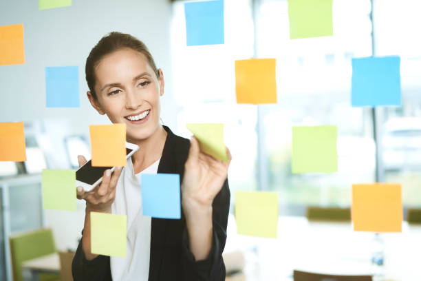 istock Young businesswoman talking on phone while looking at posting handy notes in modern office 1040931926