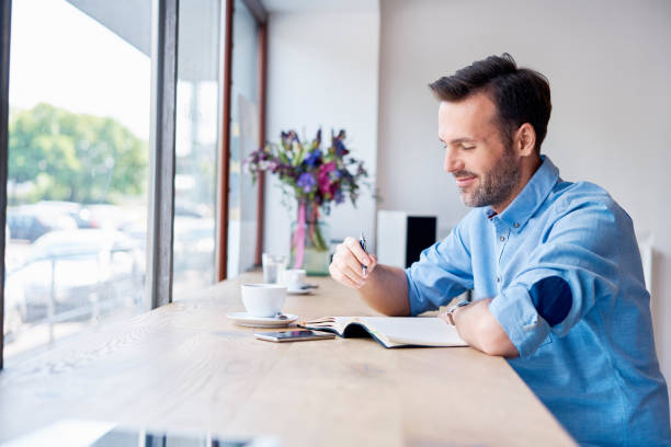 hombre sentado en la cafetería tomando café y escribir en la agenda personal - only men mid adult men men author fotografías e imágenes de stock