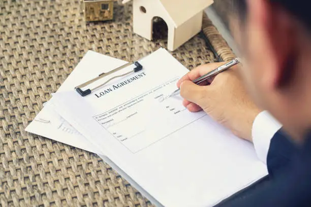 Photo of Businessman hands putting signature on document loan agreement, contract for buy new house.