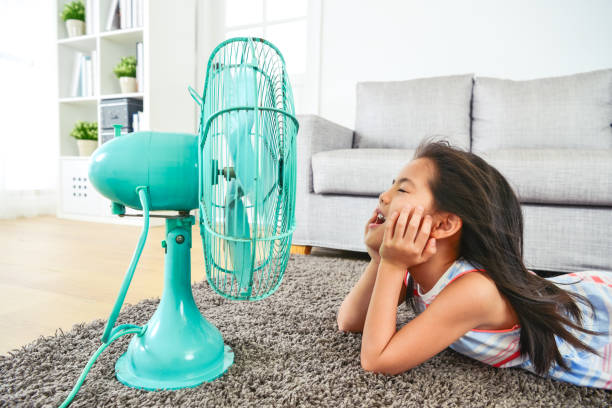 happy kid lying down in front of electric fan. happy kid lying down in front of electric fan. with eyes clossed and hair blown by the breeze. half-body view from side. japan small apartment stock pictures, royalty-free photos & images