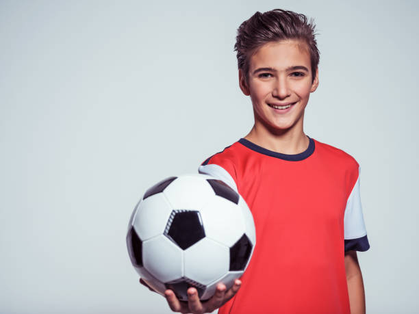 sorrindo o rapaz adolescente no sportswear segurando uma bola de futebol - soccer teenager sport adolescence - fotografias e filmes do acervo