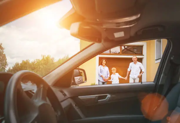 Photo of Young couple with little boy son goes to their car standing on the home yard inside car view