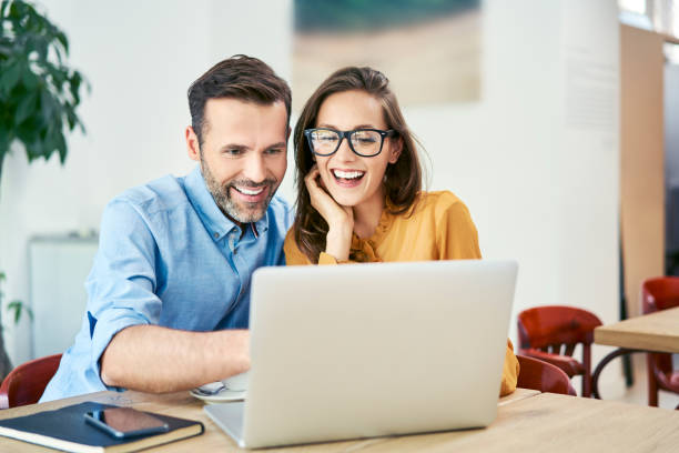 ritratto di coppia allegra che usa laptop insieme mentre è seduta al bar - couple cheerful happiness men foto e immagini stock