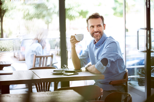 Portrait of handsome man having coffee and looking away in modern cafe