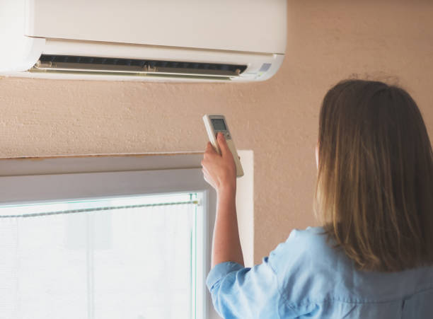 istock Woman holding remote control aimed at the air conditioner. 1040945418
