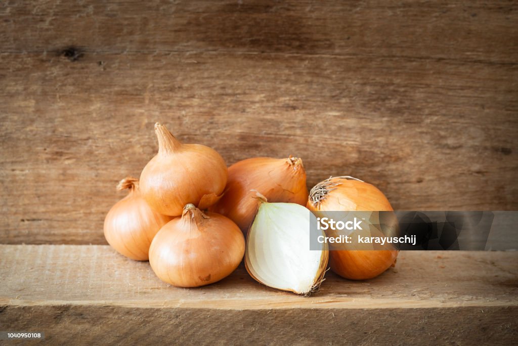 Golden Onions on a Wooden Plank A heap of fresh golden onions on a wooden plank. One onion is cut and let see the white texture vegetable Onion Stock Photo