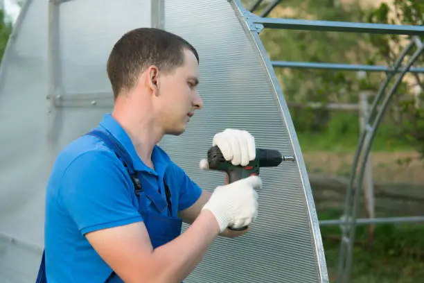 the hands of the worker twist the polycarbonate sheet with a screwdriver for installation on the greenhouse