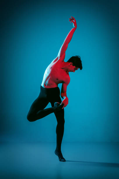 istock The male athletic ballet dancer performing dance on blue background. Studio shot. Ballet concept. Fit young man. Caucasian model 1040965292