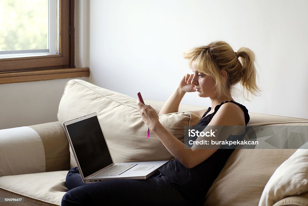 Kobieta przy użyciu telefonu komórkowego i laptopa - Zbiór zdjęć royalty-free (25-29 lat)
