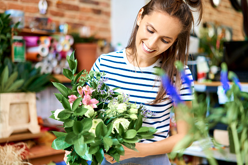 Portrait of smiling florist holding bouquet of flowers and looking at it