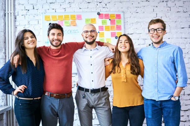 istock Cheerful students looking at camera in classroom and embracing. Group of startup businesspeople after successful launch 1040967142