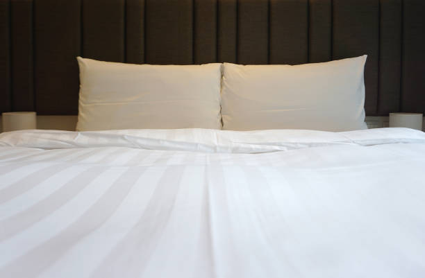 istock Double white comfortable pillows on the white bed sheet with brown headrest cushion 1040974188