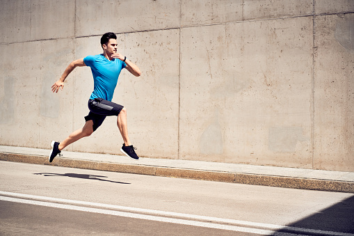 Health and fitness concept. Man doing sprinting and jumping exercises during workout session in the city
