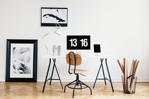 Industrial basket with kraft paper rolls and a framed poster in a white, minimalist home office interior of a freelancer architect. Real photo.