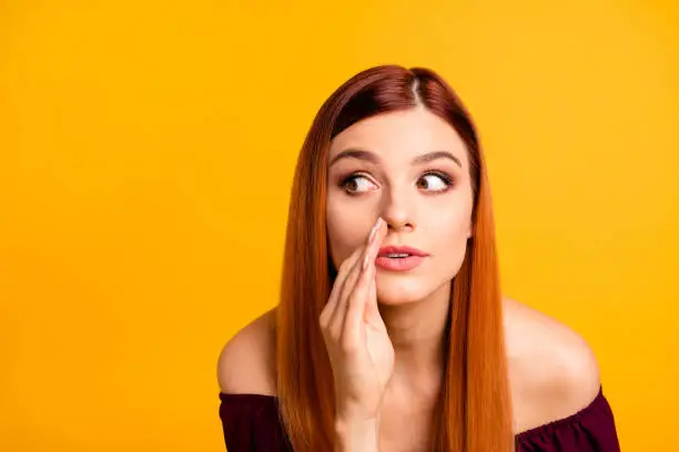 Photo of Close up portrait of  young girl tells a gossip secretly looking away and putting her hand to her mouth isolated on yellow background